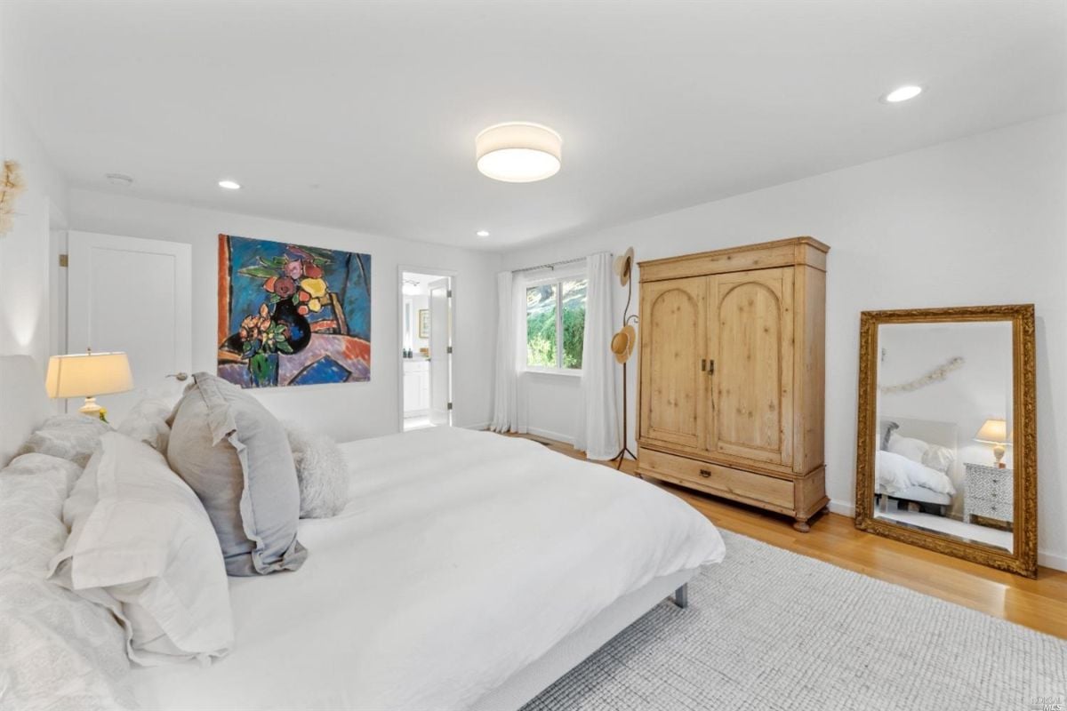 Bedroom with a large bed, wooden flooring, rug and glass windows.