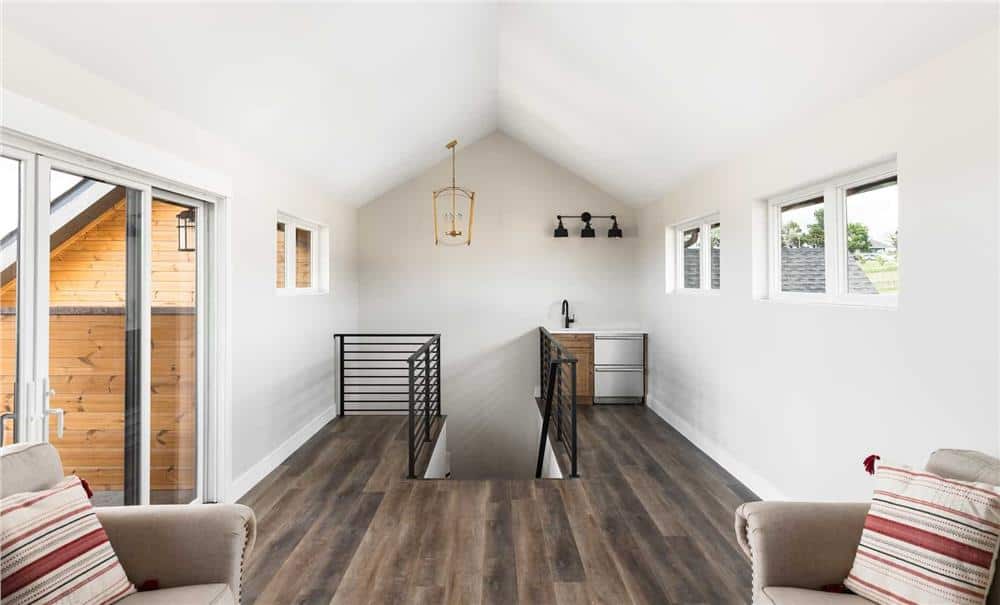 Man cave with hardwood flooring, a small bar, and beige seats under the cathedral ceiling.