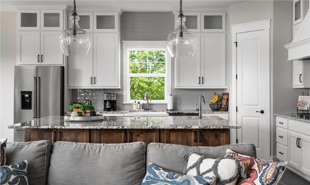Kitchen behind the great room with white cabinets. a corner pantry, and a breakfast island topped with glass pendants.