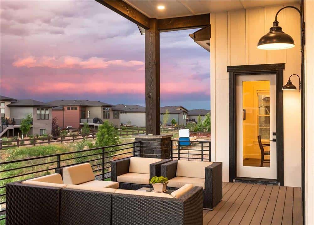 Covered deck with a glazed door and wicker cushioned chairs over the wide plank flooring.
