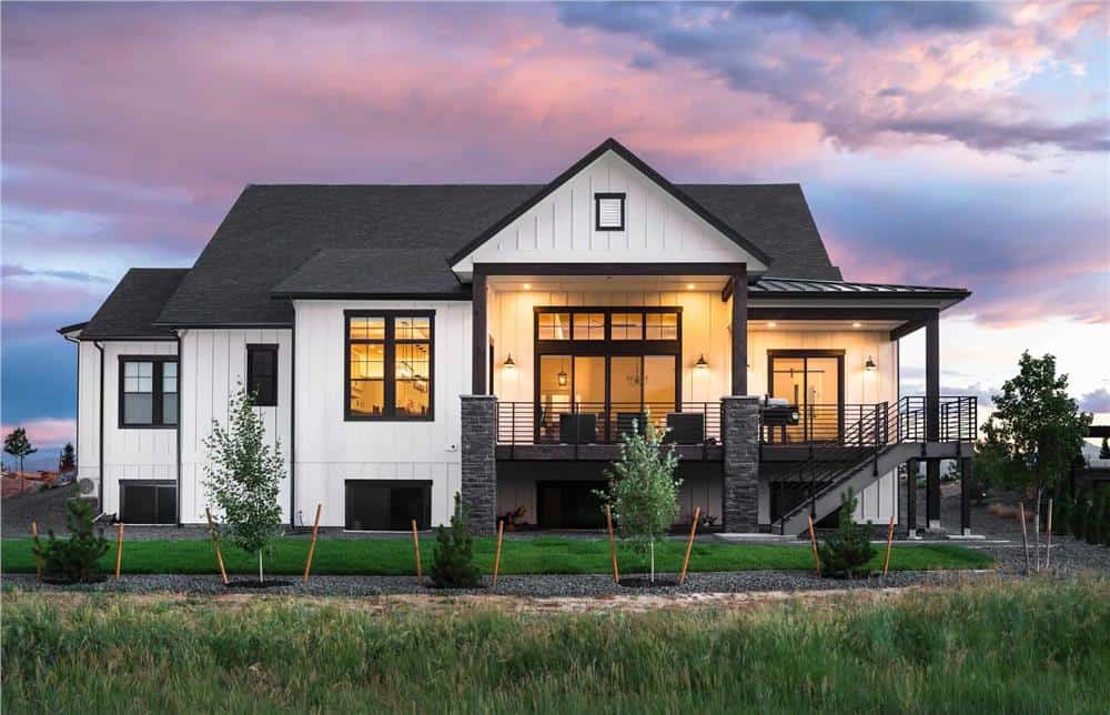 Rear view of the house showcasing the huge windows and a spacious covered deck bordered with wrought iron railings..