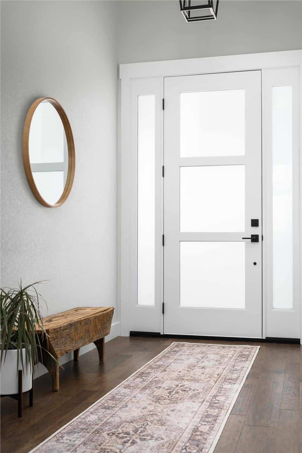 Foyer with a glazed front door, a vintage runner, and a wooden bench adorned with a round mirror.