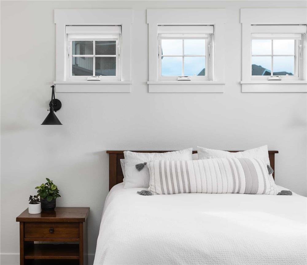 Primary bedroom with three small windows and a wooden bed complemented with a matching nightstand.