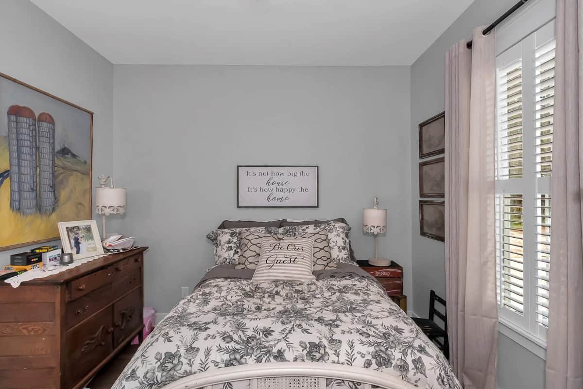 This bedroom has wooden furnishings and a louvered window that brings natural light in.