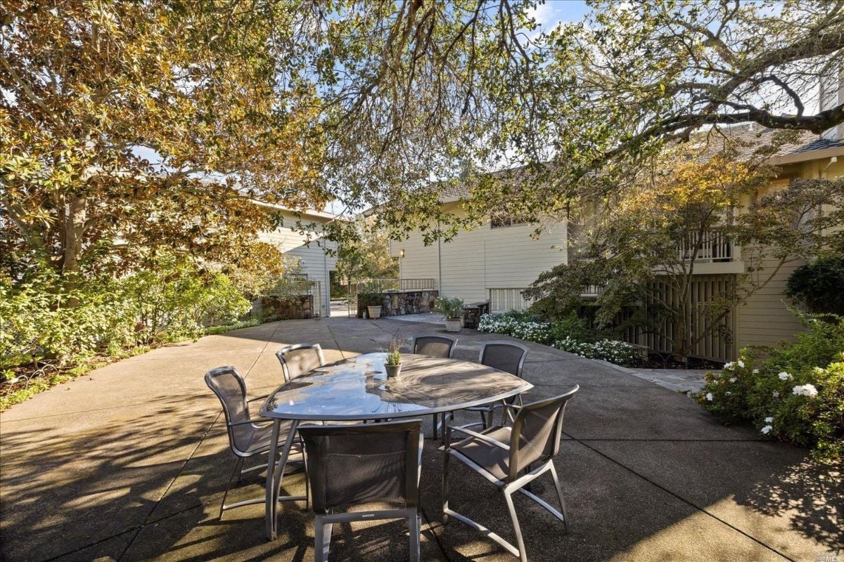 Patio under the trees with a table and chairs.