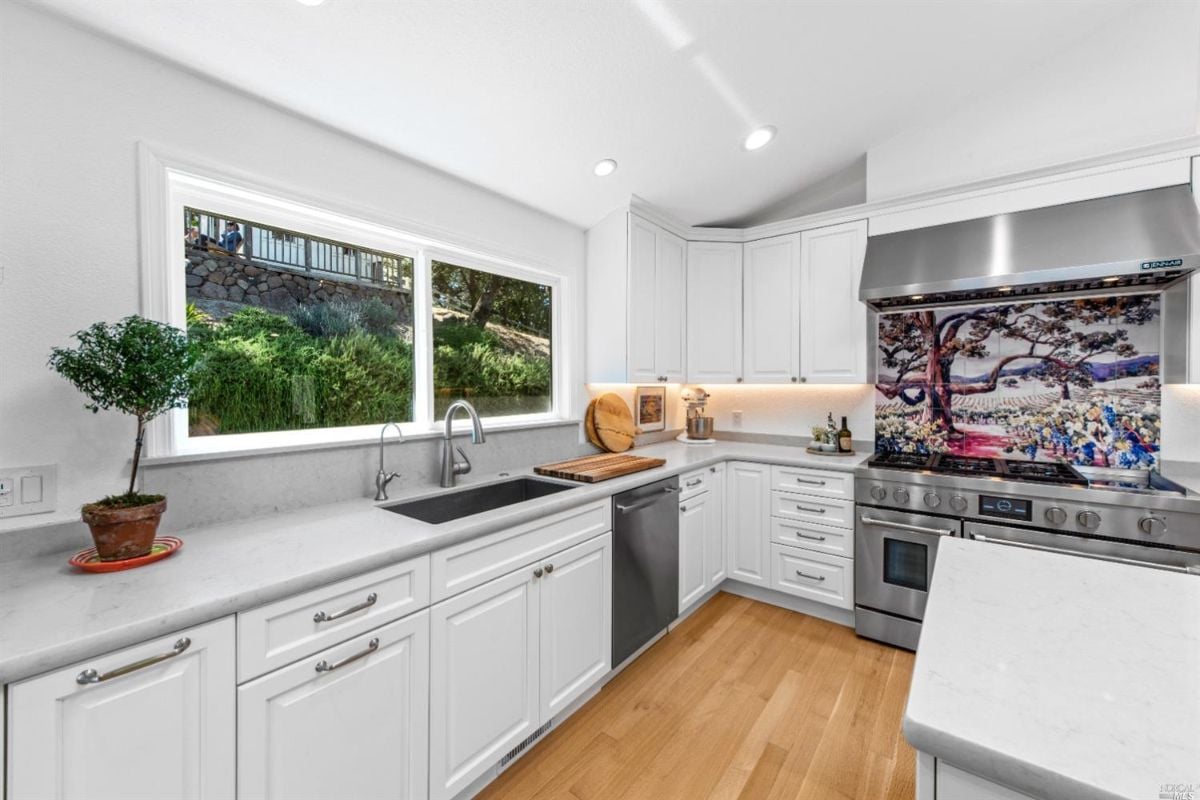 Kitchen with wood flooring, white cabinets, and custom lighting.