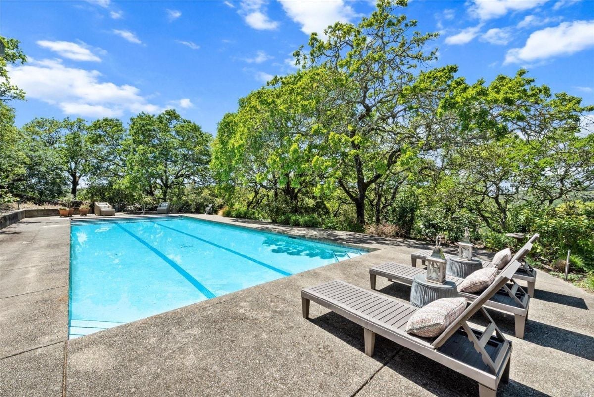 Pool with lounge chairs and trees in the background.