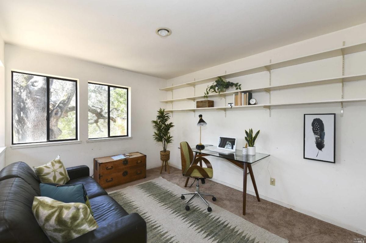 Home office with a couch, desk and glass windows.
