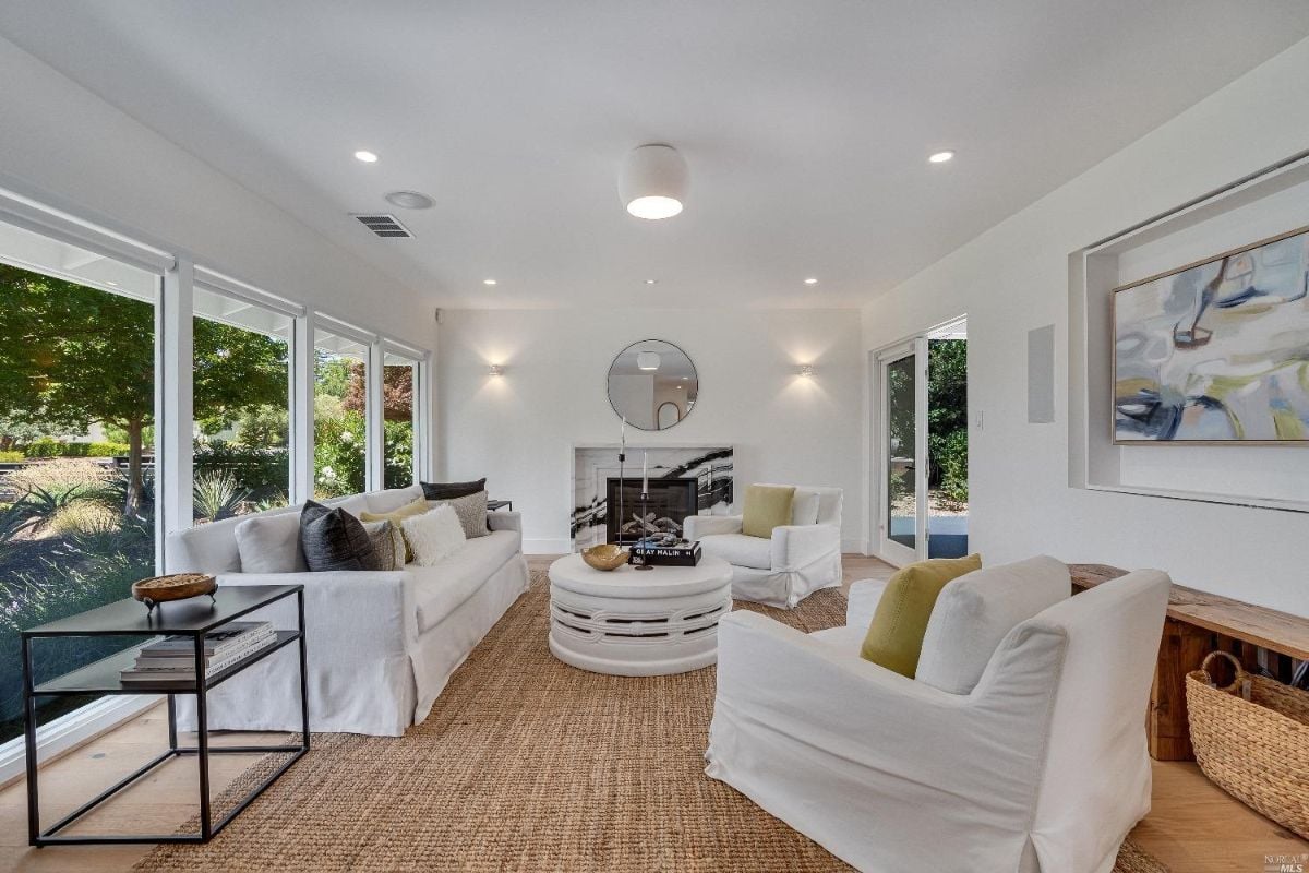 Living room with white furniture, fireplace, and large windows.