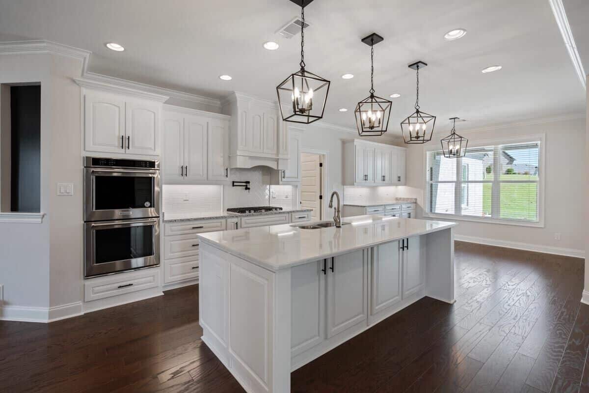 Kitchen with white cabinetry, double wall ovens, and a breakfast island topped with caged pendants.