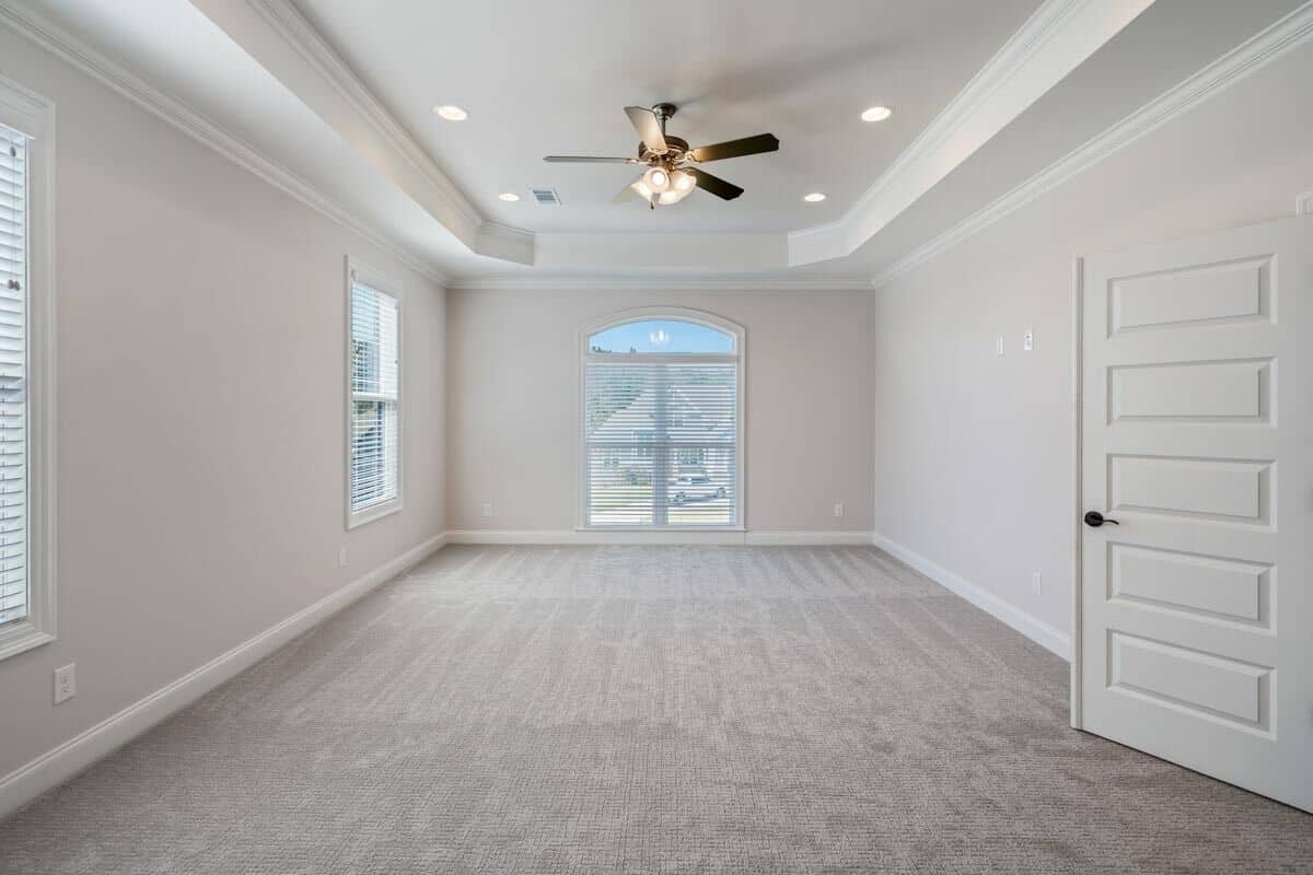Primary bedroom with carpeted floor and a tray ceiling mounted with a fan and recessed lights.