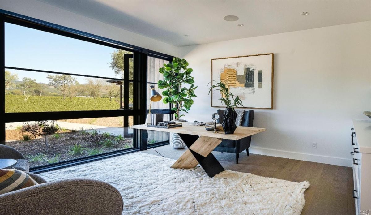 Home office with wood flooring, a rug and large glass windows.
