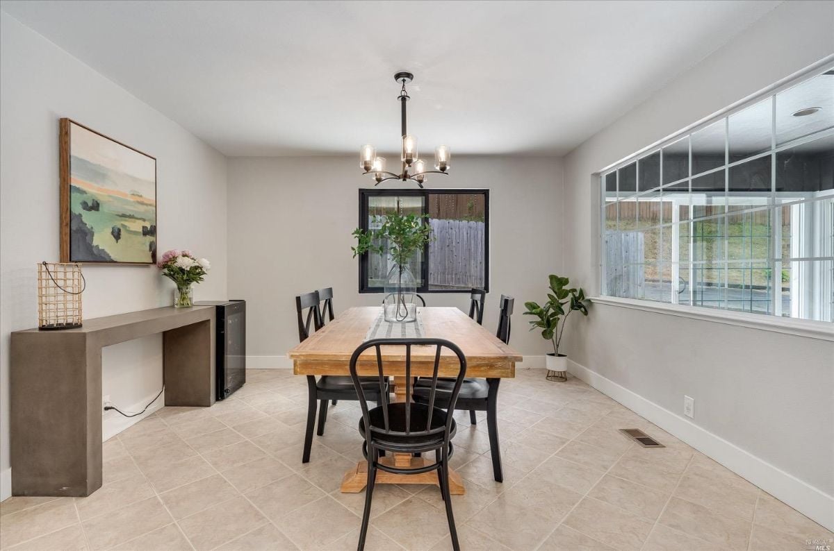 Dining room with wooden table, tile flooring, glass windows and chandelier.