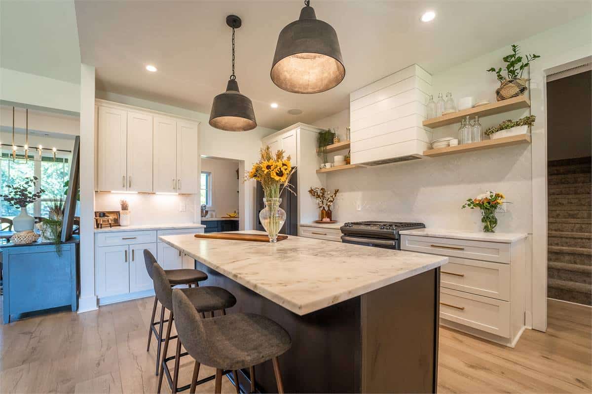 Kitchen with white cabinetry, floating shelves, marble countertops, and a breakfast island.