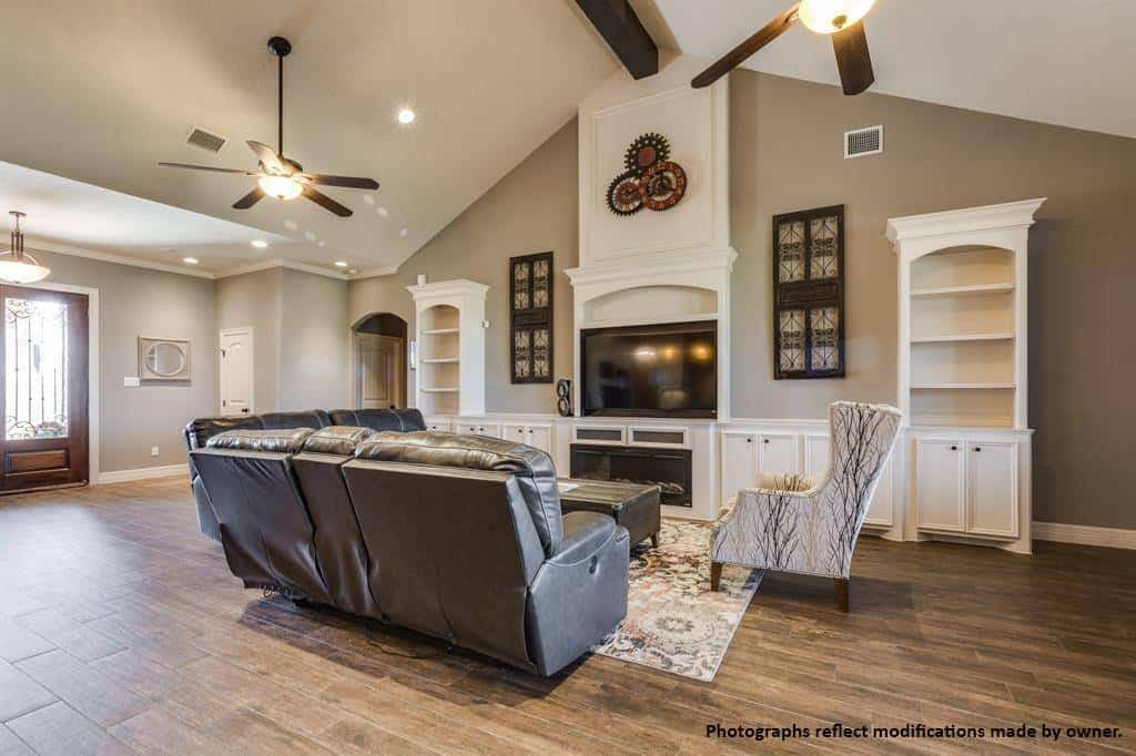 The living room has black leather sofas, white built-ins, a fireplace, and a cathedral ceiling lined with exposed beam.