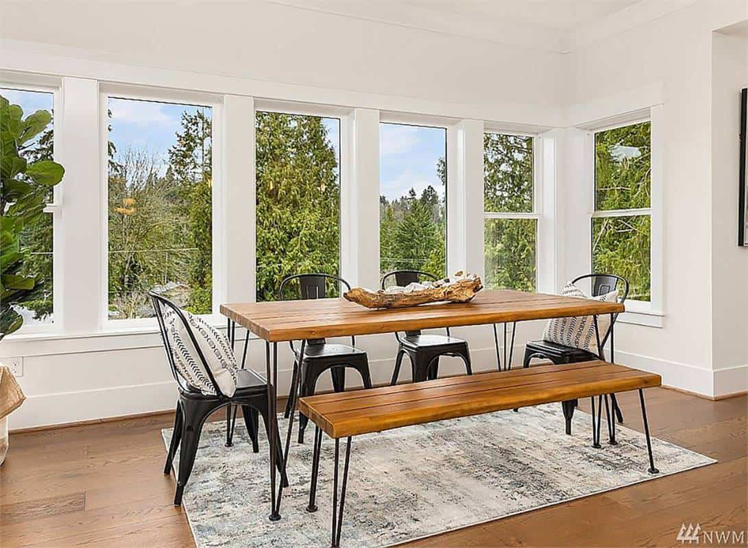 Breakfast nook with a wall of windows and a wooden dining set over a distressed area rug.