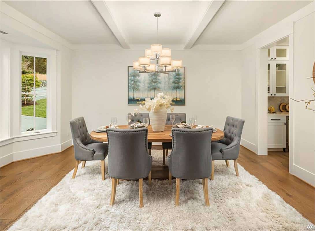 Dining room with a warm chandelier and a round wooden table surrounded by tufted chairs.