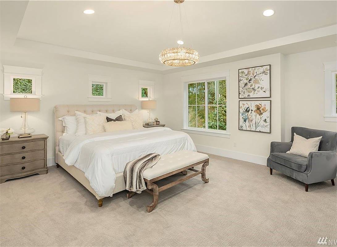 Primary bedroom with a leather tufted bed, a velvet armchair, and a round chandelier hanging from the tray ceiling.