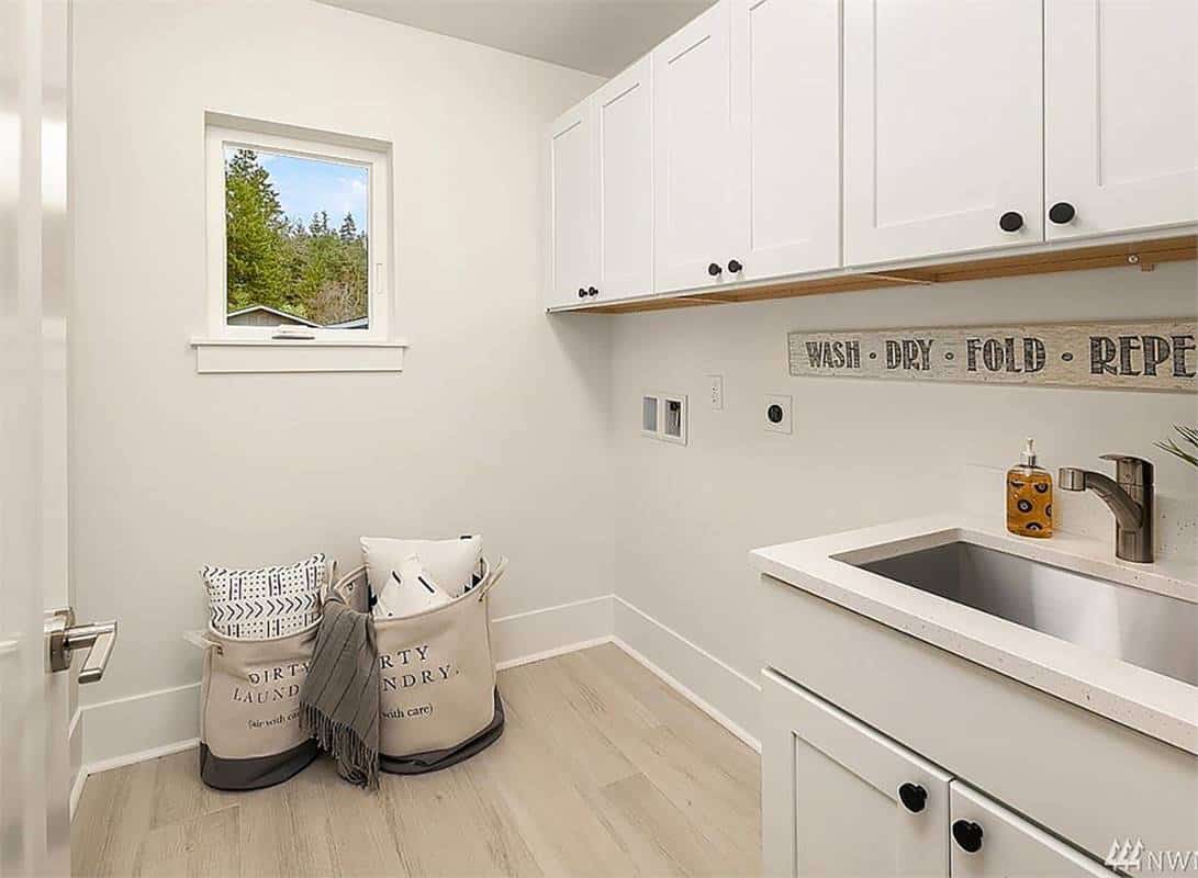 Laundry room with overhead cabinets, a large sink, and light hardwood flooring.