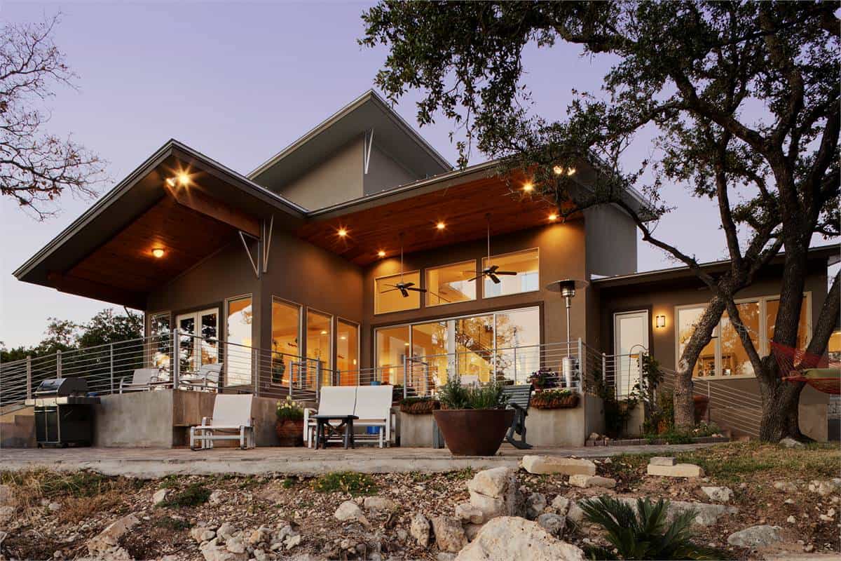 Rear view of the house with huge windows and an expansive deck framed with metal railings.