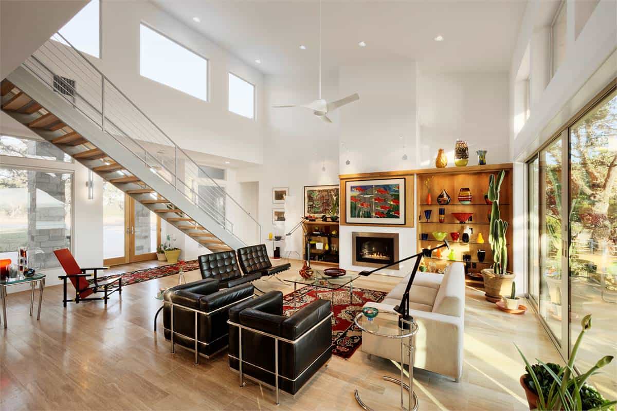 The great room has a tall ceiling, modern furnishings, and an electric fireplace flanked by wooden built-ins.