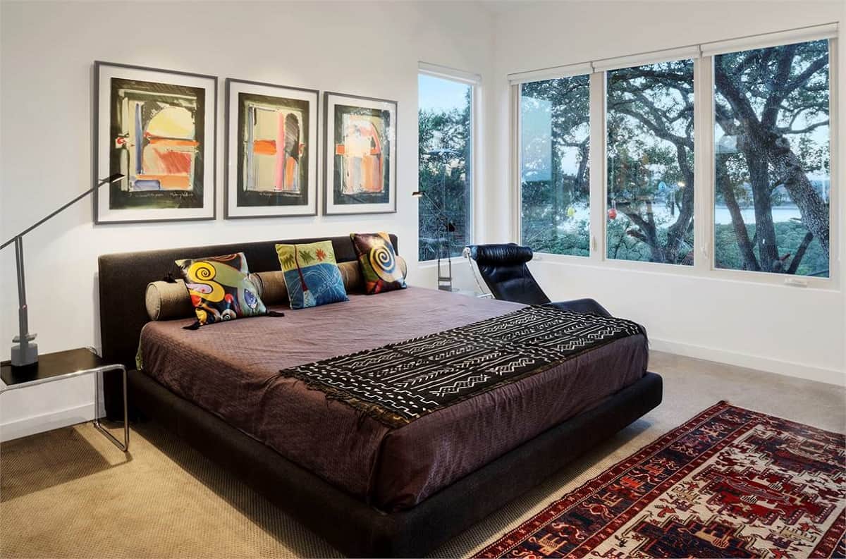 The primary bedroom offers a platform bed, a leather lounge chair, and stunning views of the lush backyard.