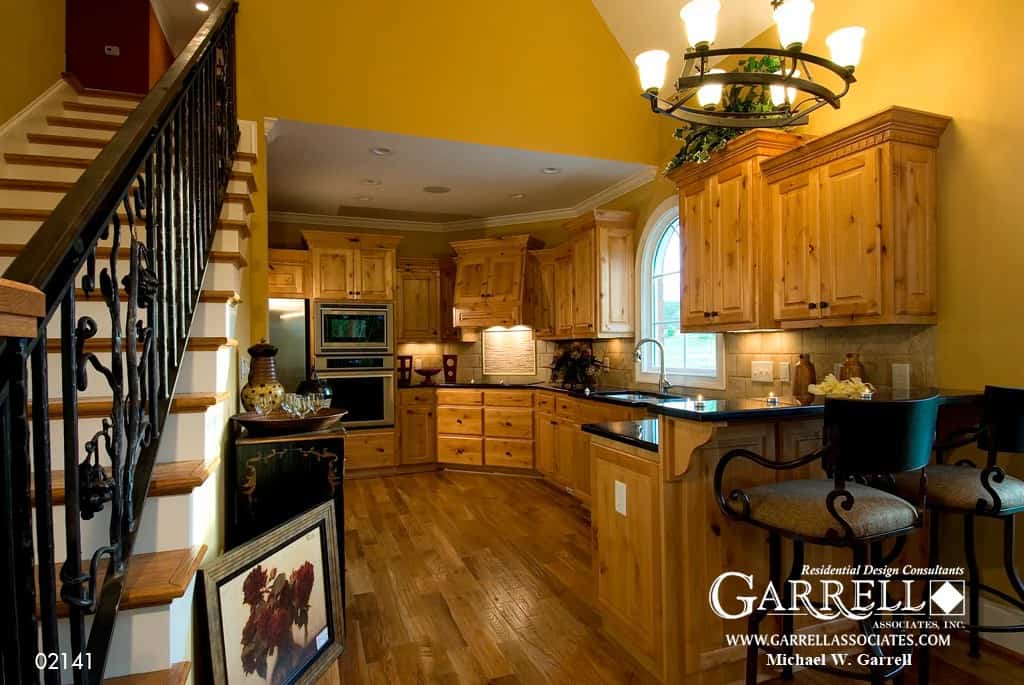 Kitchen with black countertops, a double-wall oven, and natural wood cabinetry blending in with the hardwood flooring.