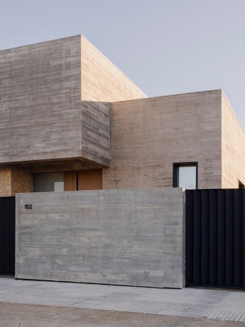 The modern house's design incorporates a sleek combination of concrete exterior and a black gate