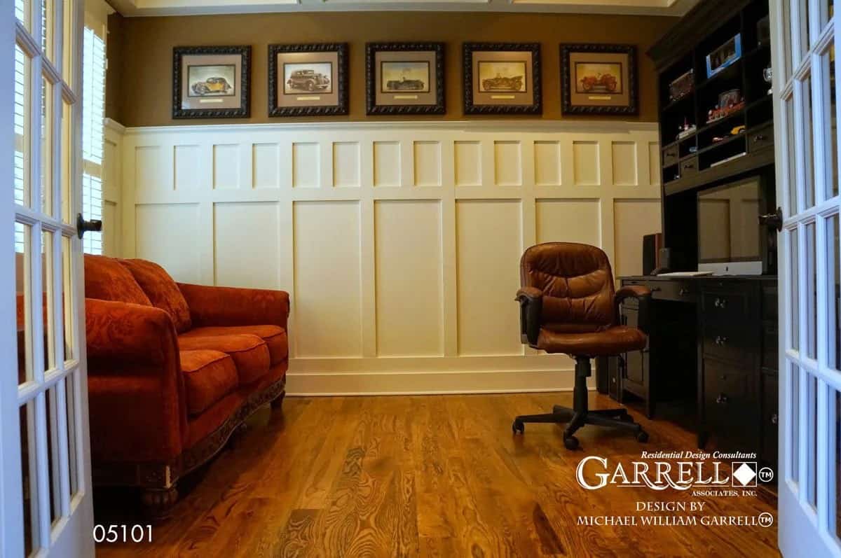 Study with a red sectional sofa, a black desk, and wainscoted walls adorned with framed artworks.