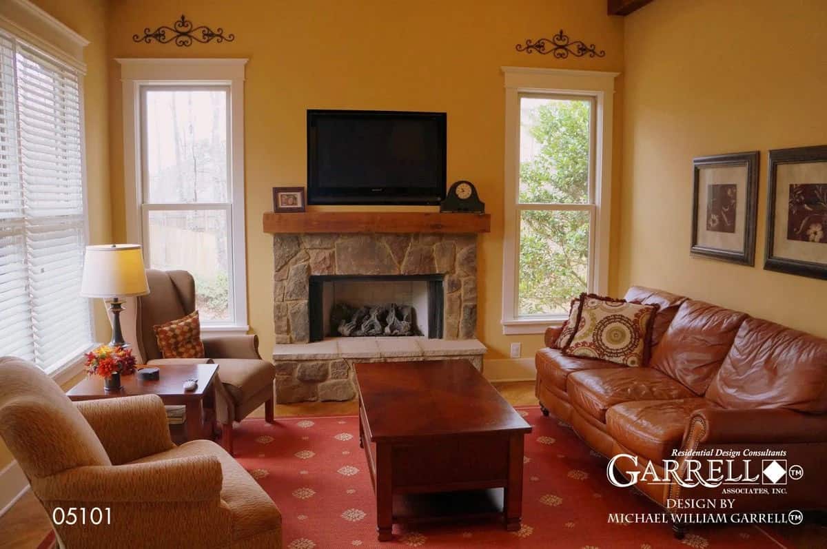 Keeping room with a leather sectional, wingback chairs, and a stone fireplace topped with a TV.