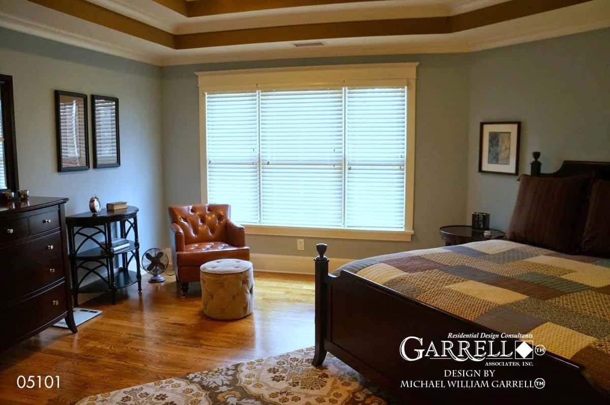 Primary bedroom with a step ceiling, a dark wood bed, matching cabinets, and a leather tufted chair complemented with a footstool.