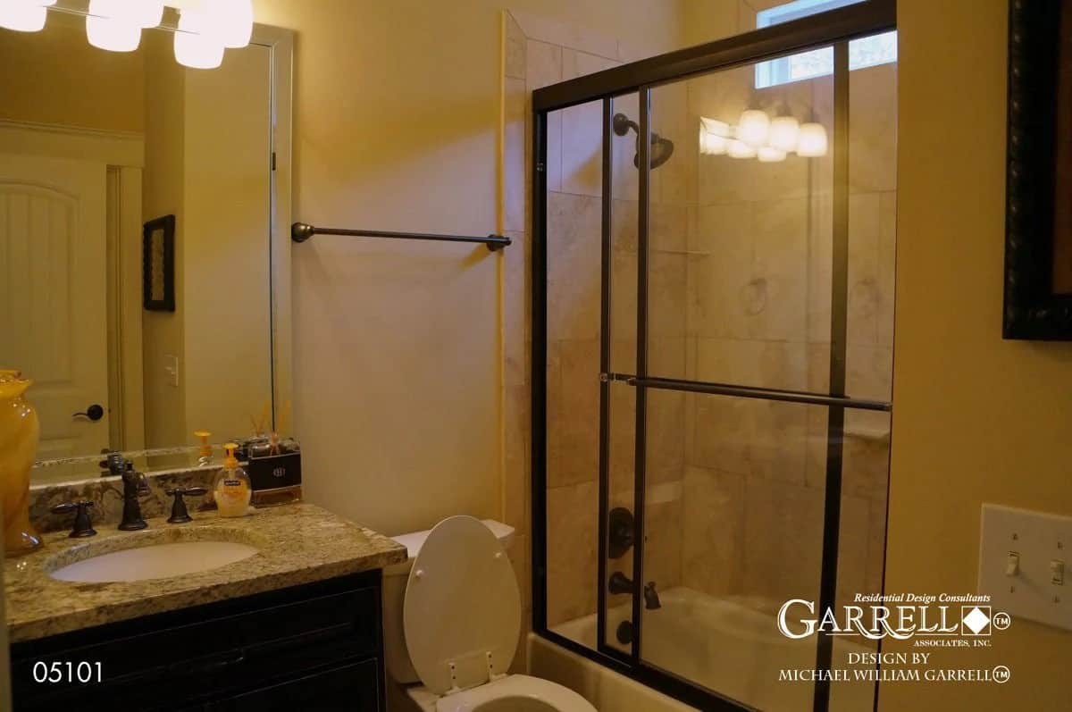 Secondary bathroom with a sink vanity, a toilet, and a tub and shower combo encased in a framed glass panel.