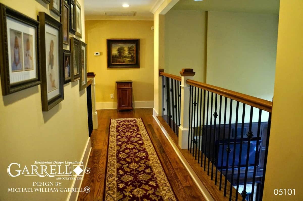 Balcony with wrought iron railings, a gallery wall, and a floral runner that lays on the hardwood floor.