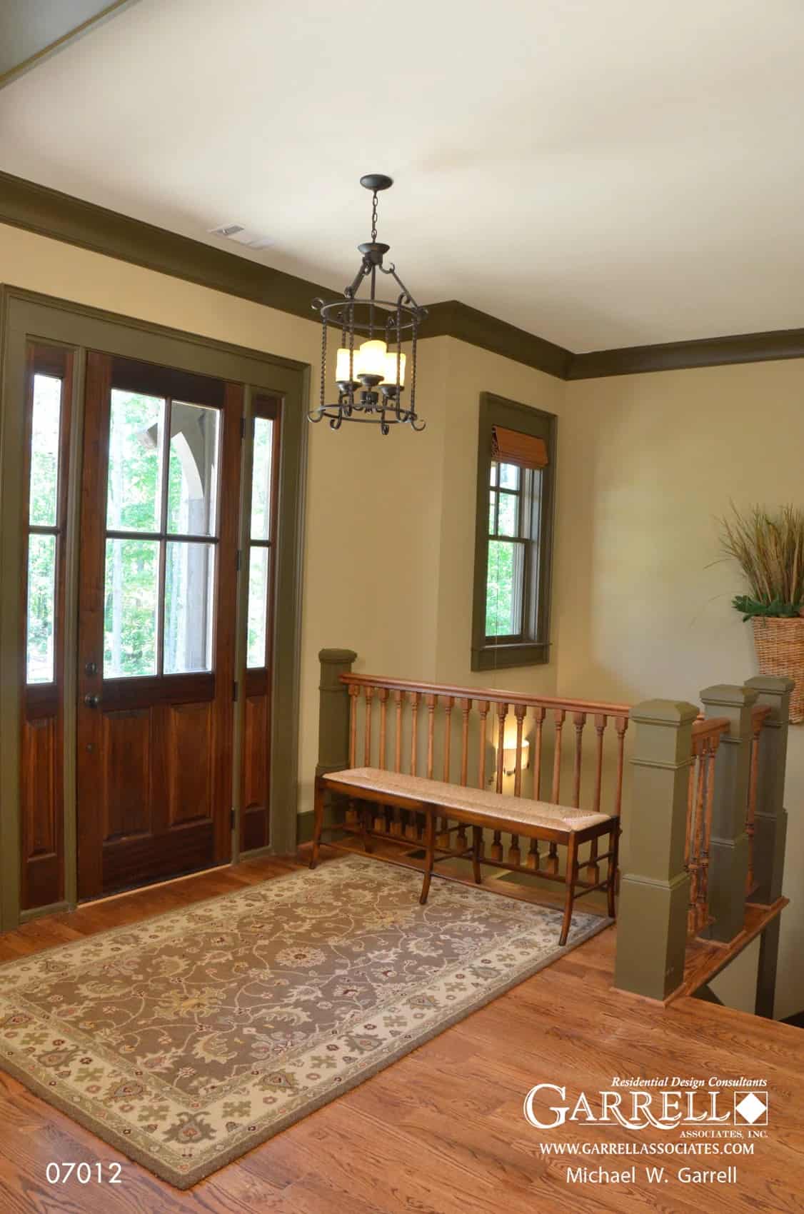 Foyer with a glazed front door, a wooden bench, and a floral rug that lays on the hardwood floor.