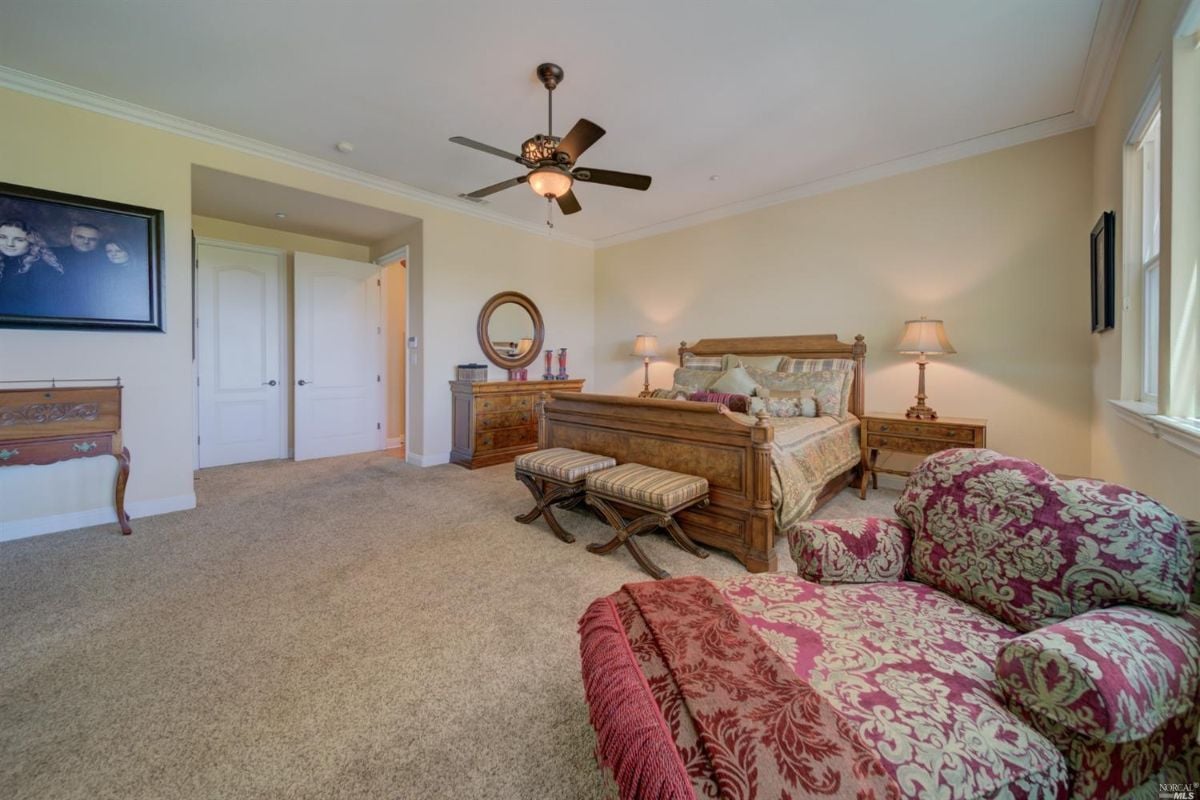 Spacious bedroom with carpet flooring, a ceiling fan, a couch, and a large bed.