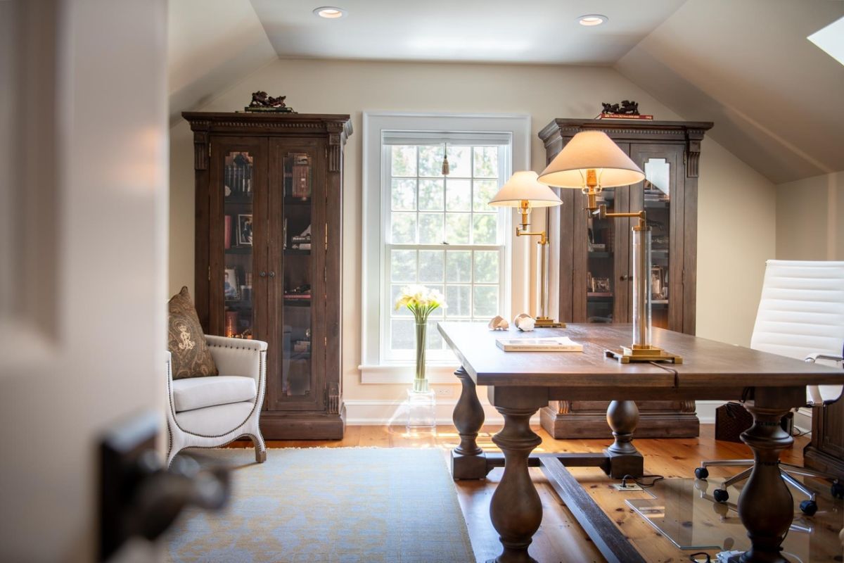 Home office with a large desk, lamps and wood flooring.