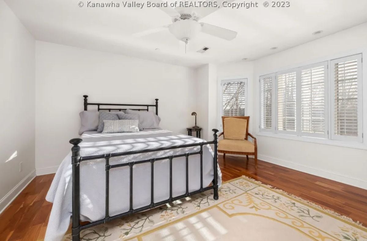 Bedroom with wood flooring, a rug, chair and a large bed.