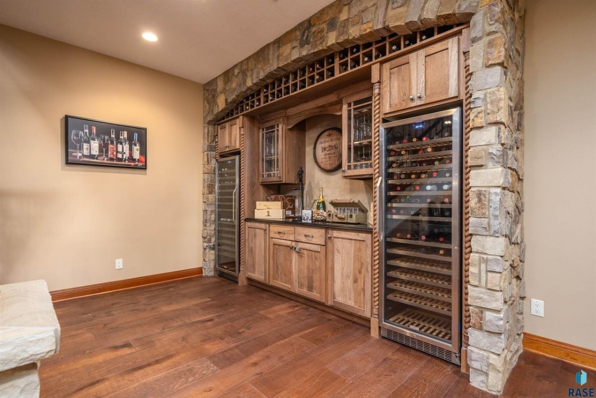 Wine cellar with custom cabinetry, a stone wall and wooden floor.