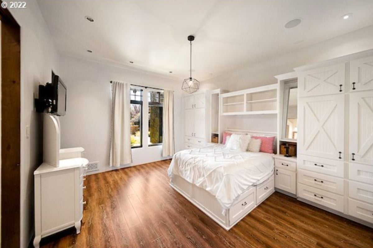 Bedroom with wood flooring, a TV, white walls and ceilings.