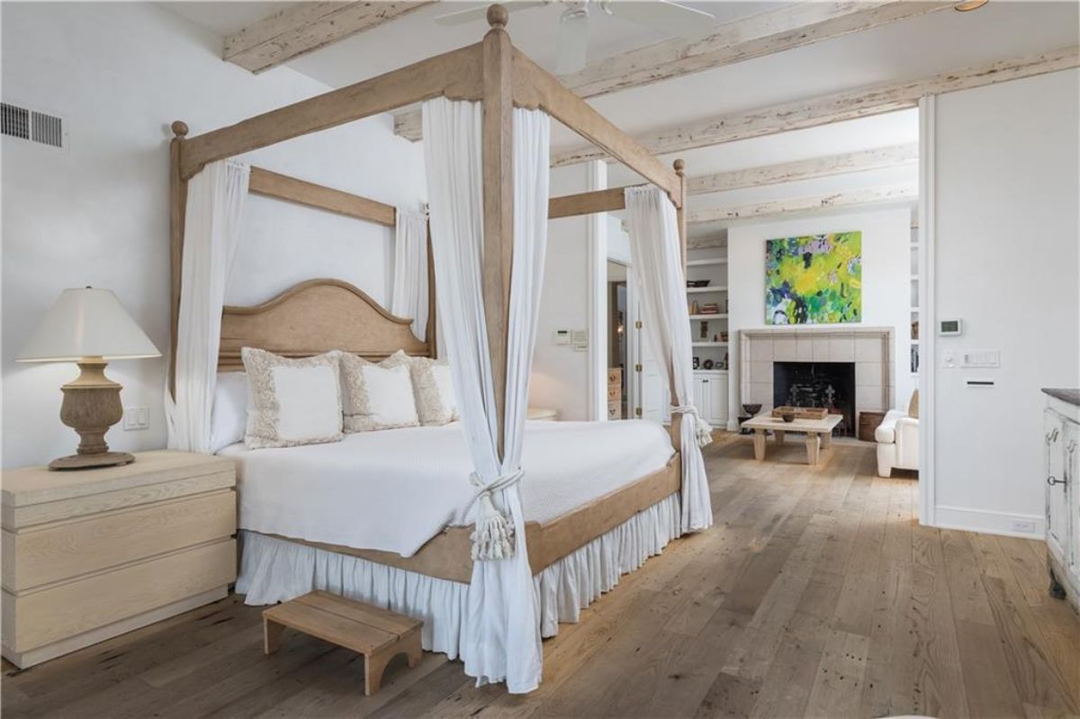 Master's bedroom with white and brown big bed and a fireplace.