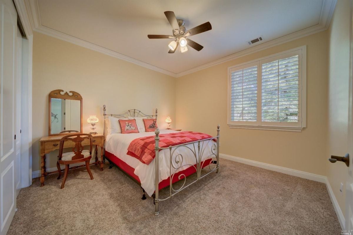 Bedroom with a carpet flooring, a large bed, and a ceiling fan.