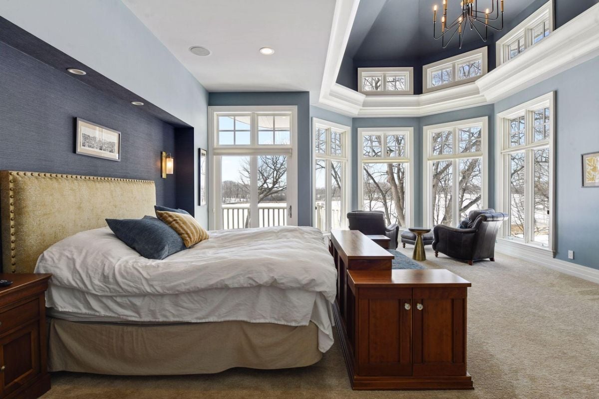 Bedroom with carpet flooring, a large bed, couches, large glass windows, and glass doors.