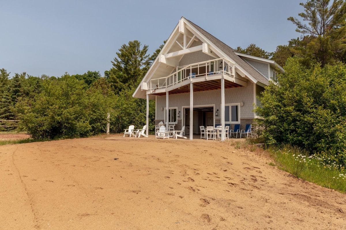 Beach house with tables, chairs, and a second level balcony.