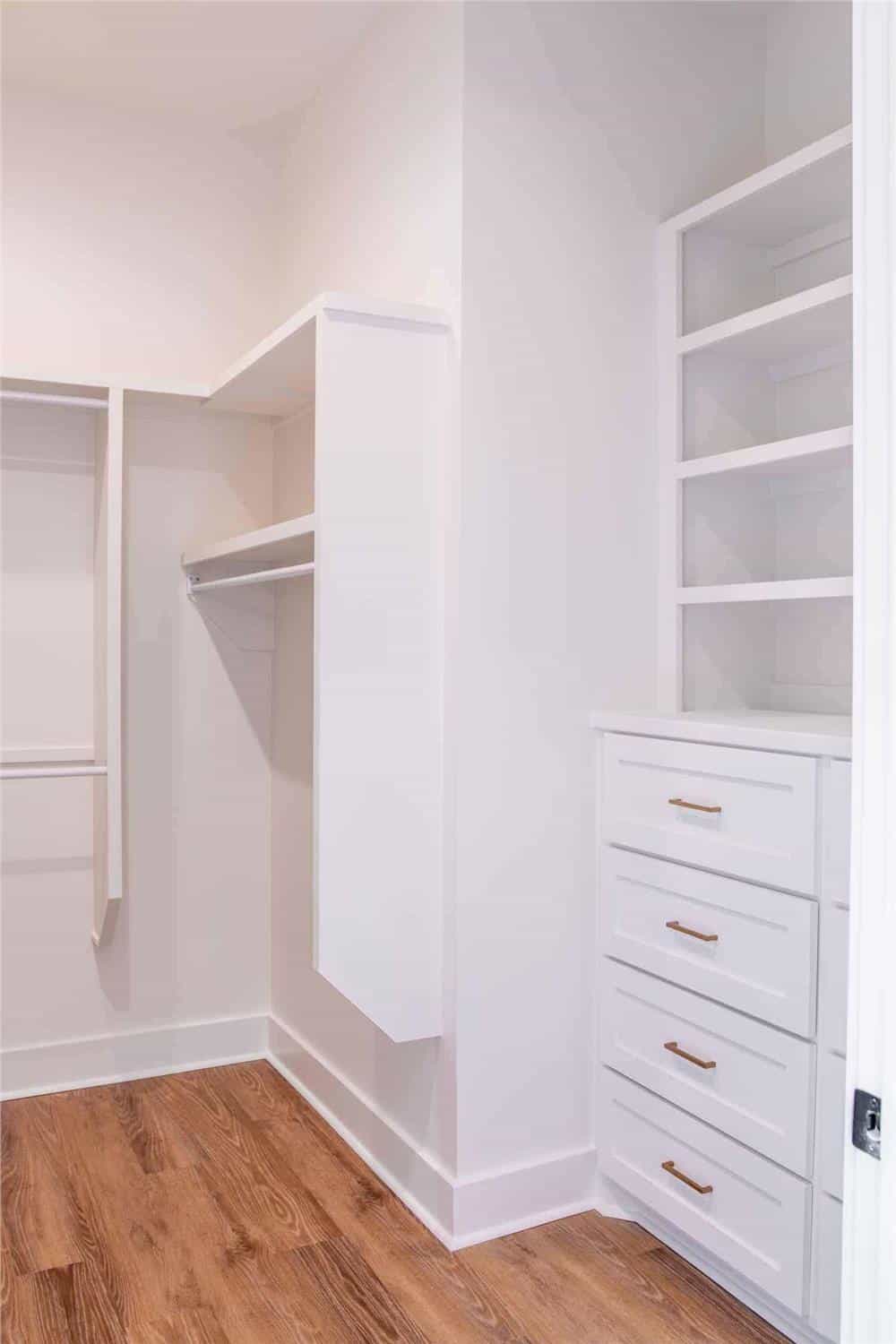Primary walk-in closet with white built-ins and hardwood floor.