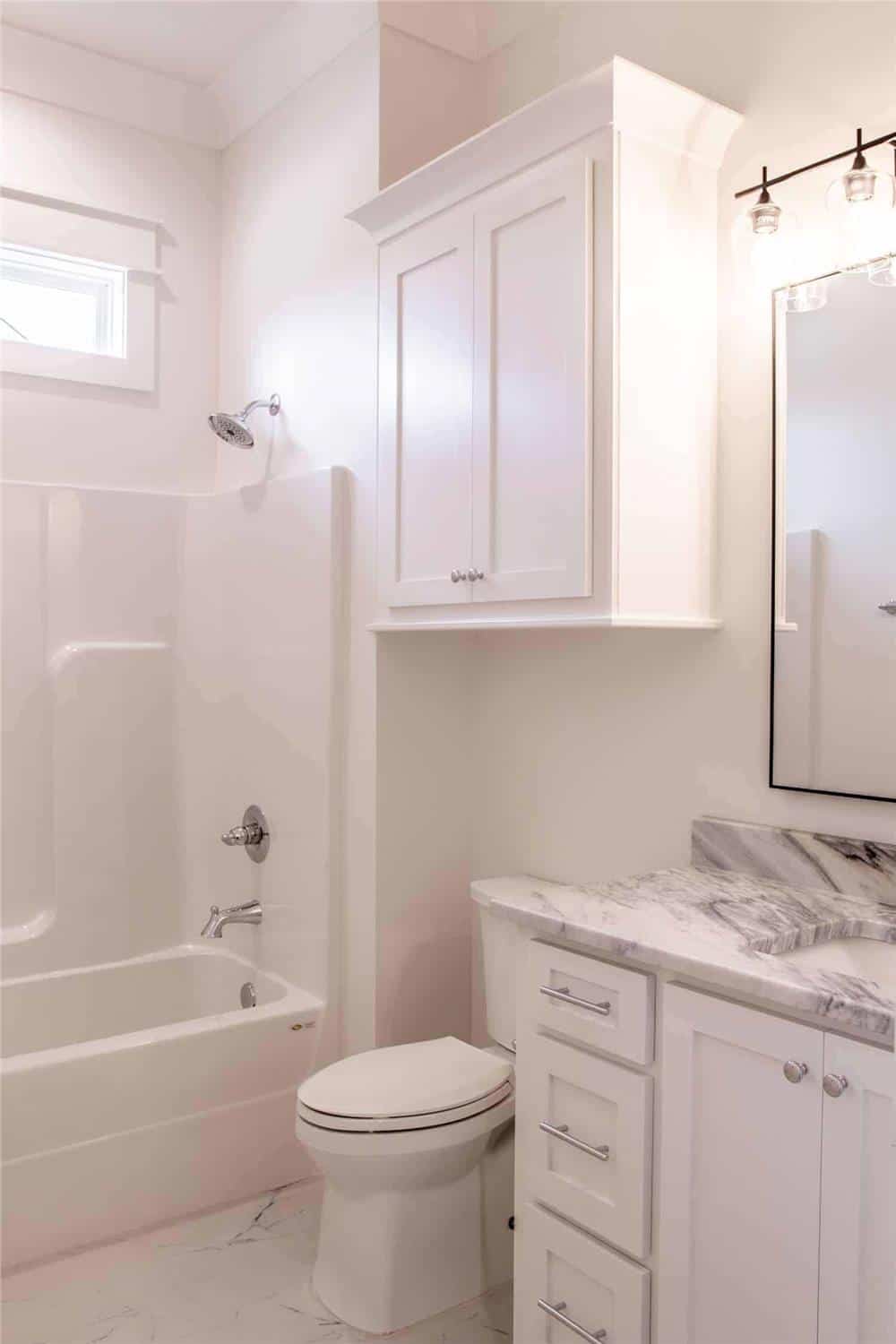 Shared bathroom with a tub and shower combo, a sink vanity, and a toilet topped with an overhead cabinet.