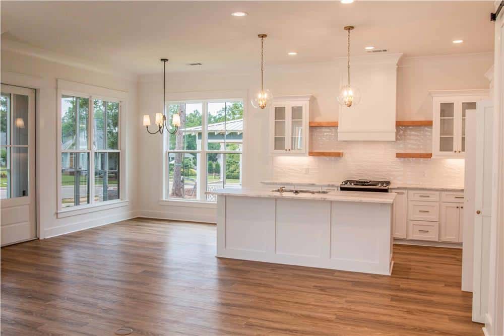 Dining area and kitchen illuminated by warm lighting fixtures and huge windows.