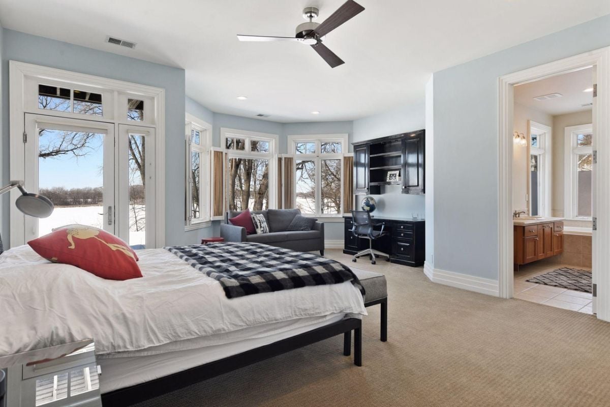 Bedroom with carpet flooring, a large bed, couches, large glass windows, and glass doors.