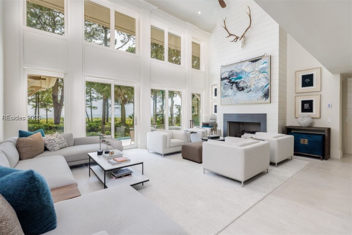 Living room with white walls, a fireplace, Cathedral ceiling, large glass windows and glass doors.