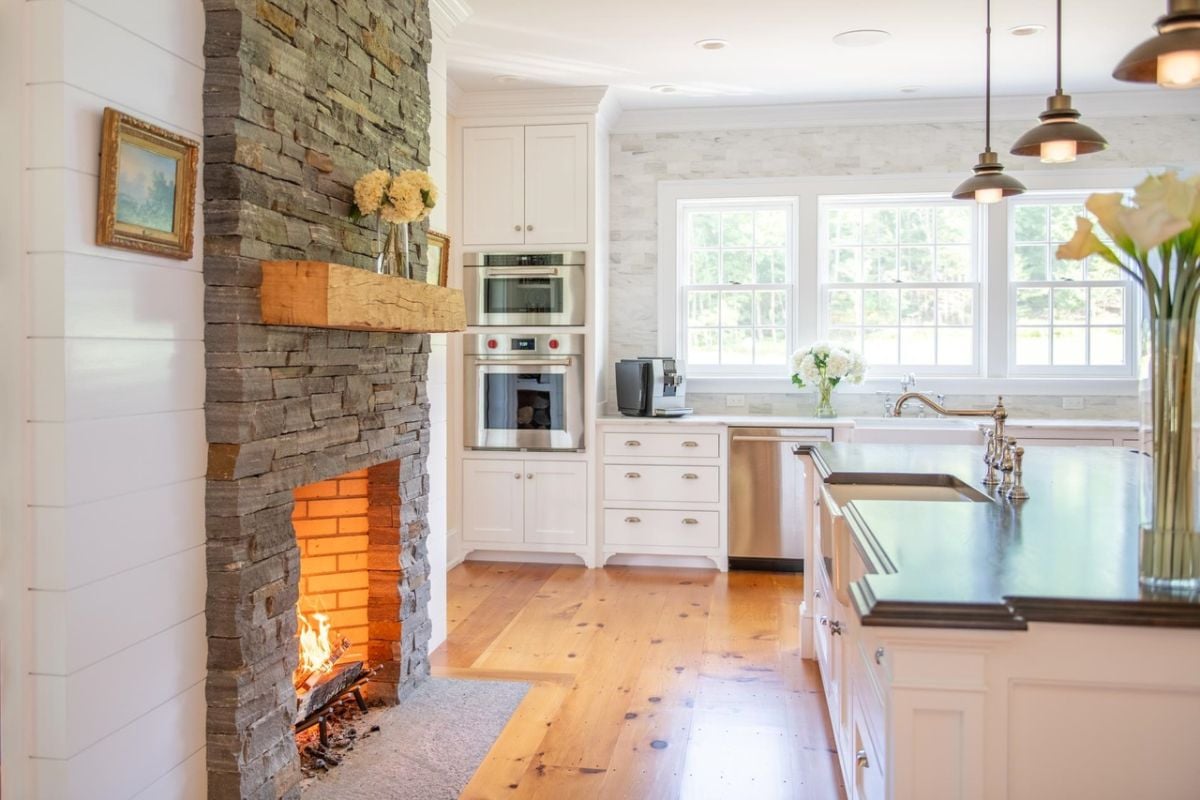 Kitchen with marble countertops, stainless appliances, painted cabinetry and a fireplace.