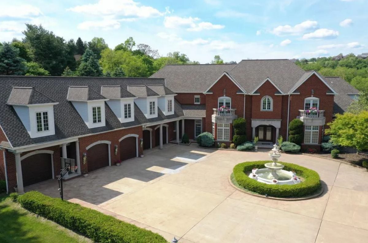 Front view of the mansion with a large driveway and a fountain.